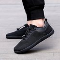 Zwarte lage sneakers met mesh bovenwerk en vetersluiting, gedragen door een model.