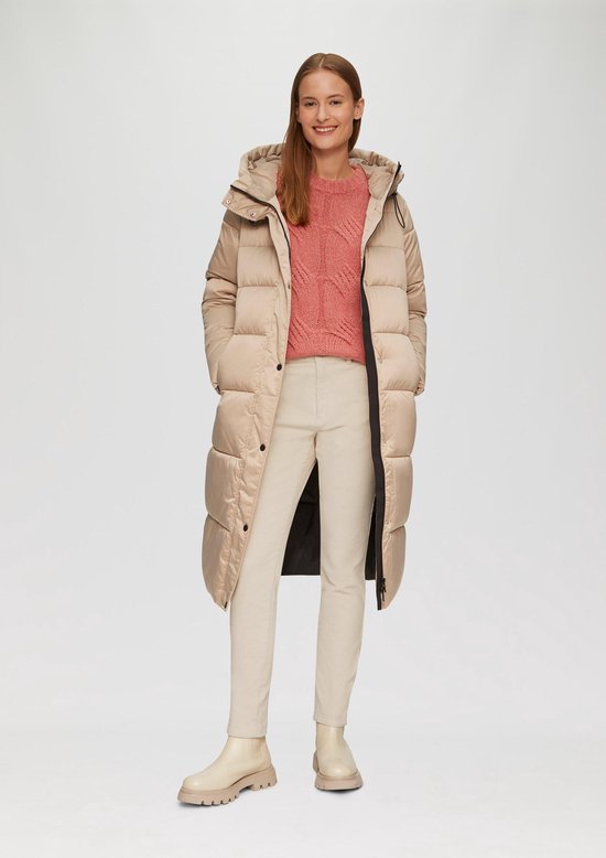 Model in een crèmekleurige corduroy broek, roze trui en beige laarsjes, met een lange beige pufferjas.