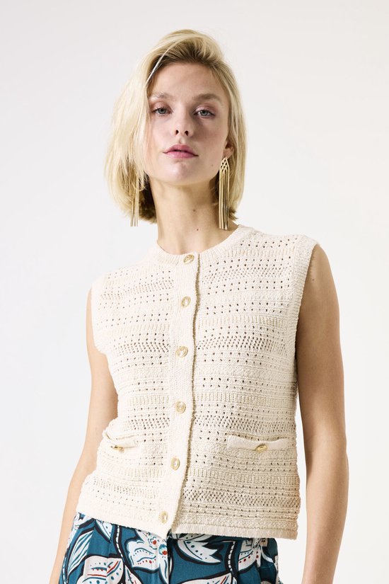 Gilet en maille crème sans manches avec boutons et poches plaquées, porté par un mannequin avec des boucles d'oreilles dorées.