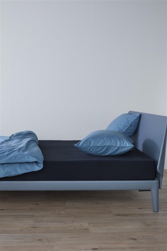 Bed opgemaakt met een marineblauw hoeslaken en lichtblauwe lakens en kussens.
