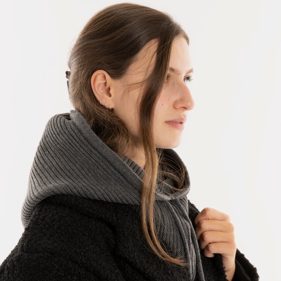 Een vrouw met lang bruin haar en een grijze gebreide colsjaal met capuchon, die over haar hoofd is getrokken.