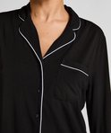 Close-up van een zwart pyjamashirt met witte biezen, borstzak en knoopsluiting.