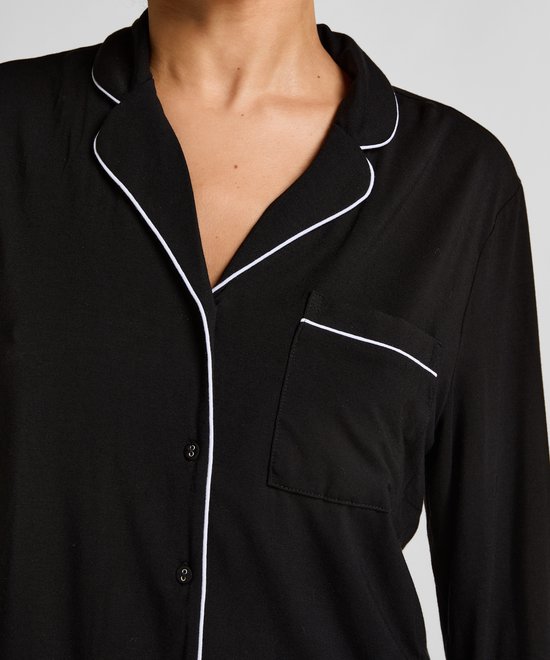 Close-up van een zwart pyjamashirt met witte biezen, borstzak en knoopsluiting.