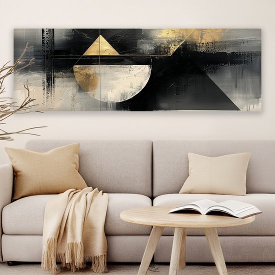 Abstract schilderij met geometrische vormen in zwart, wit en goud, hangend boven een bank.