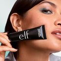 Model met turquoise oogschaduw houdt een zwarte e.l.f. Power Grip Matte Primer tube vast.