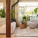 Ronde houten bijzettafels naast een beige bank met gestoffeerde rug en een grijze fauteuil.