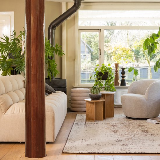 Ronde houten bijzettafels naast een beige bank met gestoffeerde rug en een grijze fauteuil.