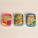 Trois boîtes à lunch Mepal remplies : crackers, légumes et sandwichs.