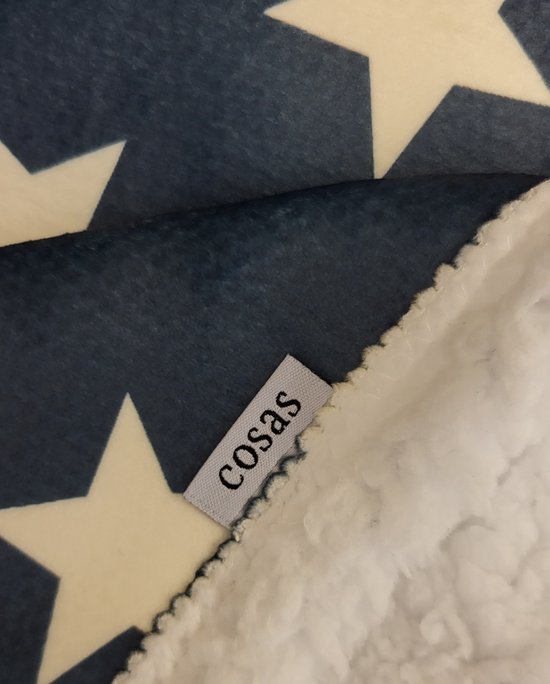 Detail van een blauwe deken met witte sterren, met label 'cosas' en witte Sherpa-stof.