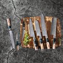 Zes Japanse messen met damastpatroon en unieke handvatten van hout en blauwe epoxy, liggend op een houten snijplank met groene peper.