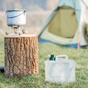 Opvouwbare jerrycan met groene kraan op de voorgrond, met kampeeruitrusting op een boomstronk op de achtergrond.