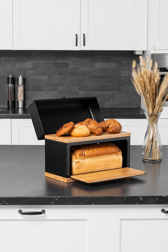 Boîte à pain noire ouverte avec du pain et des croissants, planche à découper en bambou.