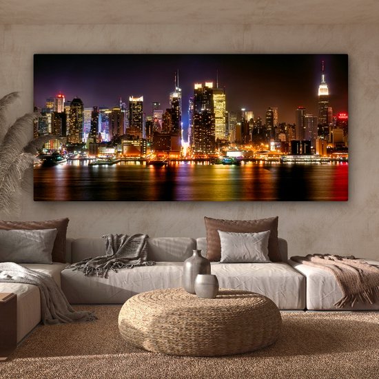 Un salon clair et moderne avec un canapé modulaire gris et une large toile de la skyline de New York la nuit.