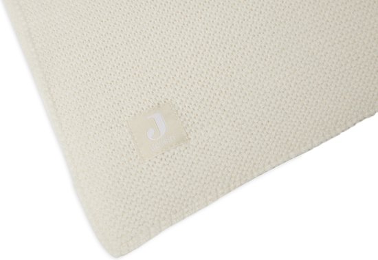 Plan détaillé d'une couverture en maille crème avec une étiquette Jollein.