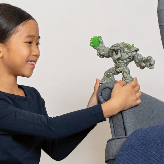 Een meisje met een donkerblauwe trui kijkt glimlachend naar een stenen monster figuur dat ze vasthoudt.
