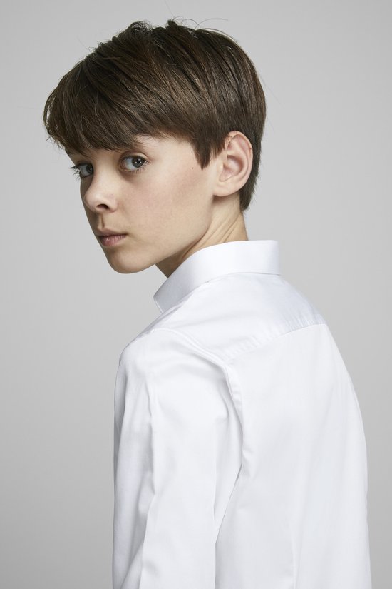 Un garçon aux cheveux bruns courts, porte une chemise blanche à manches longues.