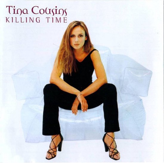 Tina Cousins zit op een witte bank in een zwarte outfit met hakken.