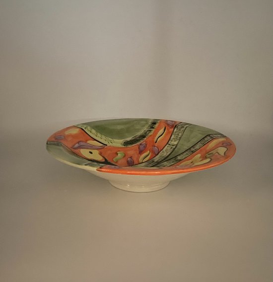 Vue latérale d'un plat de service vert et orange avec des motifs décoratifs.