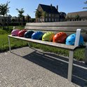 Sept casques PRO SPORT LIGHTS colorés sur un banc en bois: rose, rouge, vert, bleu, jaune, orange, bleu clair.
