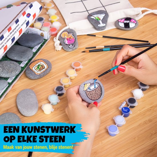 Tafel met stenen, potjes verf, penselen, en beschilderde stenen met sushi en cocktail.