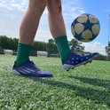 Homme sur terrain vert avec un ballon de football, portant des chaussettes vertes et des chaussures.