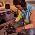 Man met een kleurrijke hoodie, luisterend naar muziek met een zwarte DJ-koptelefoon.