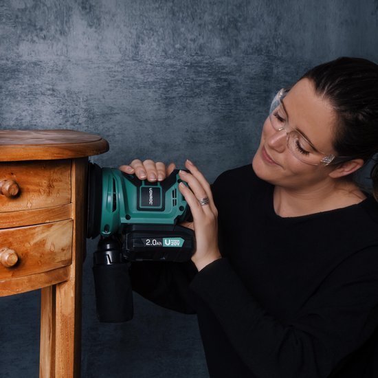 Vrouw met veiligheidsbril schuurt een houten meubel met een groene Vonroc excentrische schuurmachine.