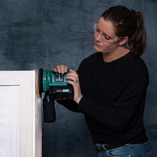 Vrouw met veiligheidsbril schuurt een wit meubel met een groene Vonroc excentrische schuurmachine.
