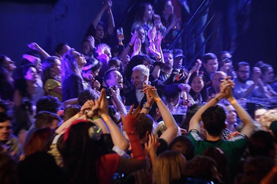 Een menigte juicht in een club met blauw licht, met mensen die klappen en bier vasthouden.