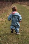 Jongen in groen regenpak met visgraatpatroon rent over grasveld.