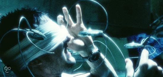 Close-up van Tom Cruise's hand met een horloge, omringd door blauwe lichten en draden.