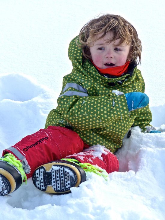 Jongen in de sneeuw, met een groene jas met sterrenprint en rode broek.