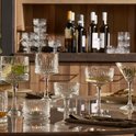 Set van diverse kristallen glazen op een gedekte tafel, waaronder cocktailglazen met een gedetailleerd patroon.