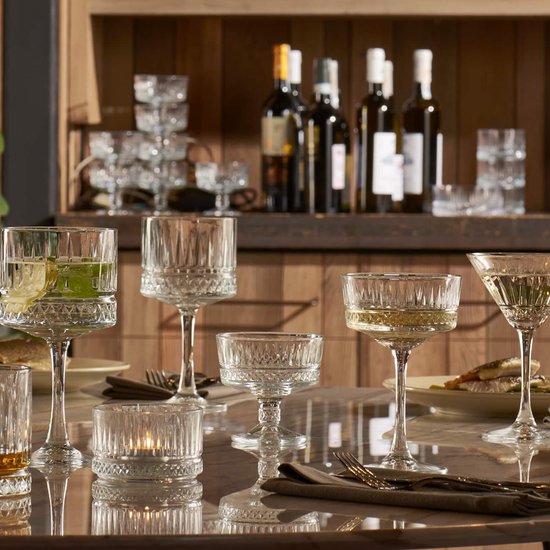 Set van diverse kristallen glazen op een gedekte tafel, waaronder cocktailglazen met een gedetailleerd patroon.