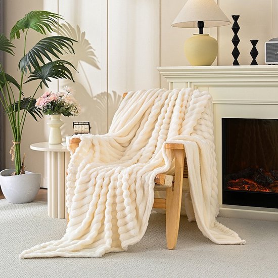 Een crème kleurige, zachte plaid met ribbelpatroon, gedrapeerd over een houten stoel in een woonkamer.