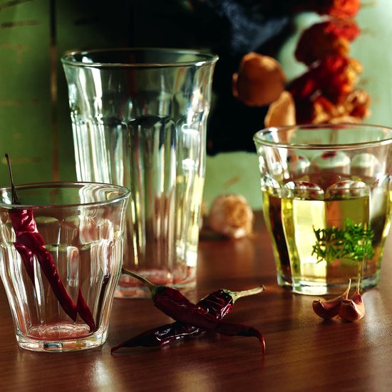 Trois verres Duralex Picardie transparents avec cannelures verticales, deux remplis de liquide jaune et de piments séchés, un vide.
