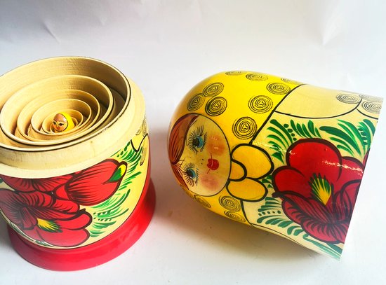 Open Matroesjka pop met kleinere poppen erin en een losse pop ernaast, beschilderd met gezichtjes, rode bloemen en gele details.