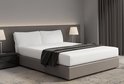 Un lit double avec une base grise, des draps blancs, deux oreillers blancs et un jeté gris foncé.