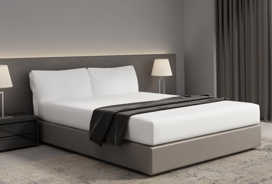 Un lit double avec une base grise, des draps blancs, deux oreillers blancs et un jeté gris foncé.