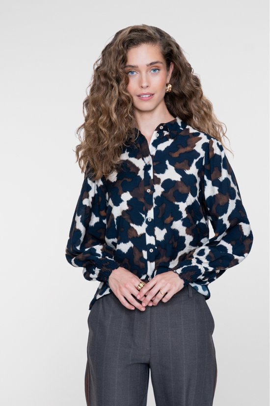 Model draagt een blouse met een blauw, bruin en crème abstracte print, lange mouwen met gesmokte boorden en een kraag.