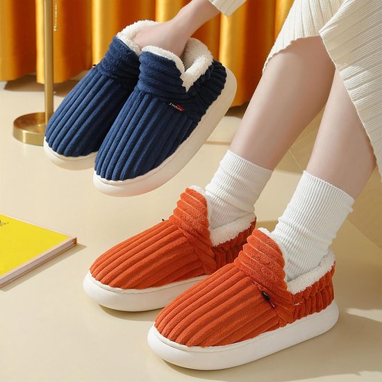 Voeten met witte sokken dragen oranje geribbelde sloffen met witte zool, blauwe versie in de hand.