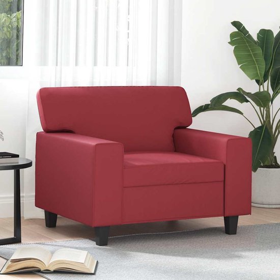 Wijnrode kunstleren fauteuil op donkere pootjes, met een bijzettafel, plant en open boek ernaast.