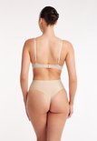 Achteraanzicht van een model in een beige, naadloze high-waist string en bh.