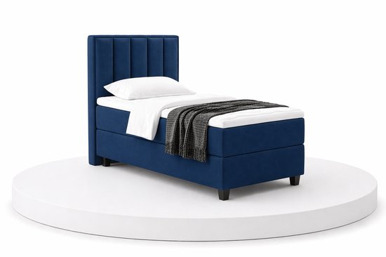 Eenpersoons boxspring in donkerblauw, met een gestoffeerd hoofdbord en een gebreide plaid.
