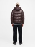 Rug van model in donkerbruine gewatteerde jas met capuchon en een zwarte joggingbroek.