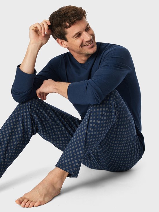 Zittende man in donkerblauwe pyjamaset met broek voorzien van een streepjespatroon.