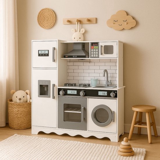 Witte speelgoedkeuken met grijze accenten, magnetron, fornuis, wasmachine en koelkast. Houten krukje en mand met knuffelbeer ernaast.