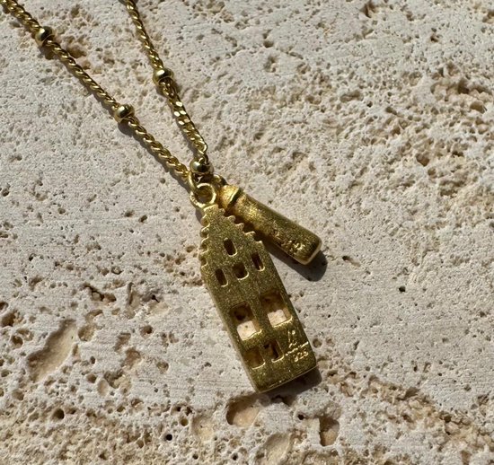 Goudkleurige ketting met hanger in de vorm van een Amsterdams grachtenpandje op een stenen ondergrond.
