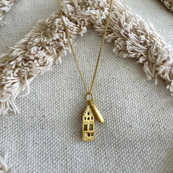 Goudkleurige ketting met hanger van een Amsterdams grachtenpand op een witte textiele achtergrond.