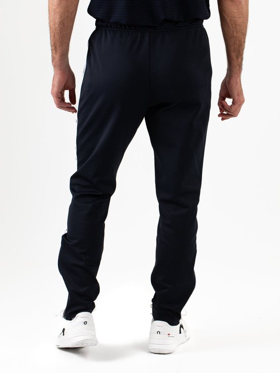 Aanzicht op de achterkant van een marineblauwe Sjeng Sports trainingsbroek met witte zijstrepen.